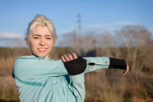 A beautiful young blonde woman sitting in the grass and stretching in a park with elbow brace