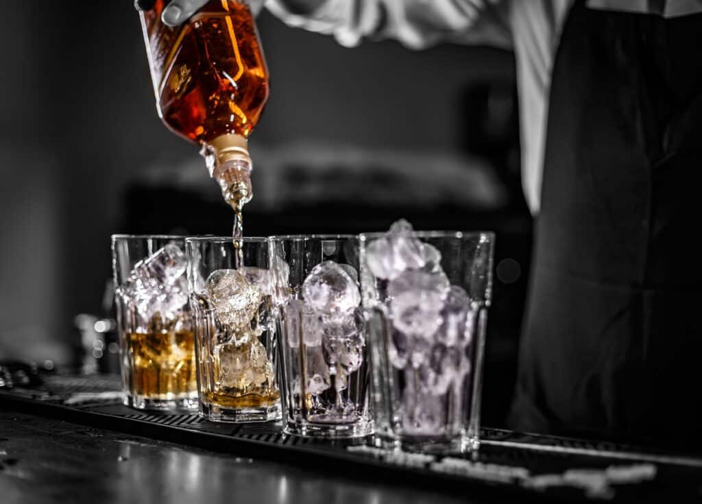 Barman pouring alcoholic drink into the glasses with ice cubes on the bar counter