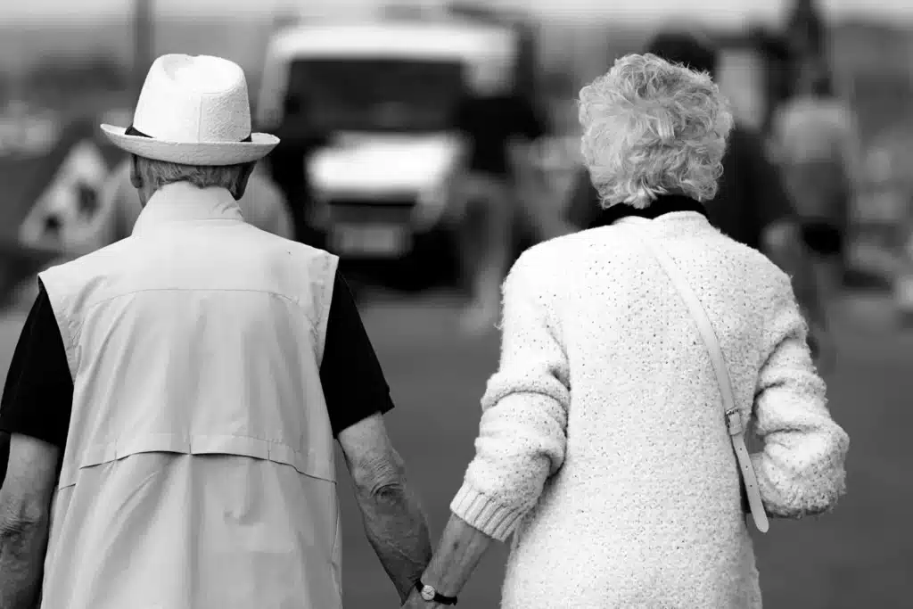 A black and white image of the backs of an older couple walking together.