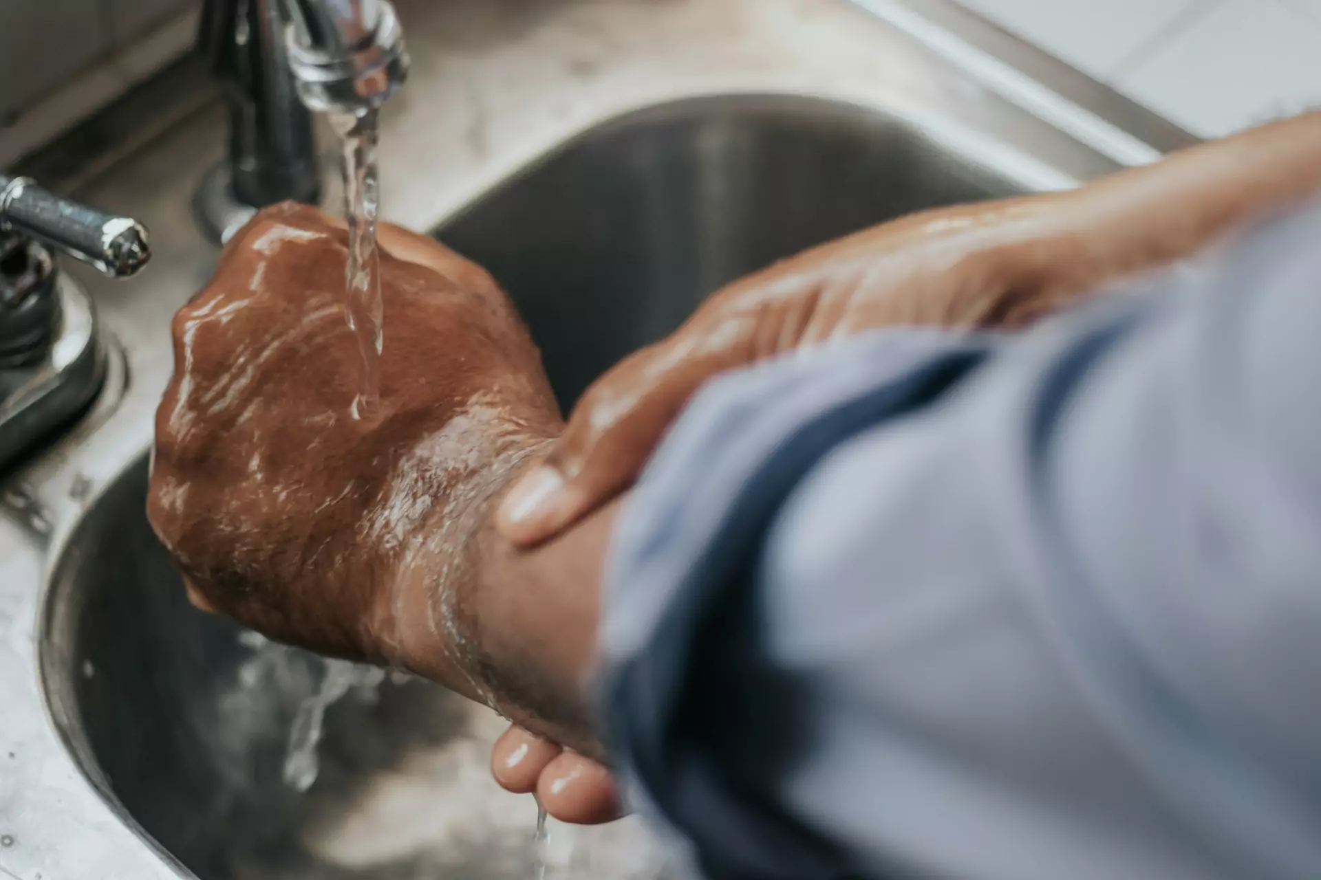 A person holding their hand under running water after suffering a burn. First aid for burns.