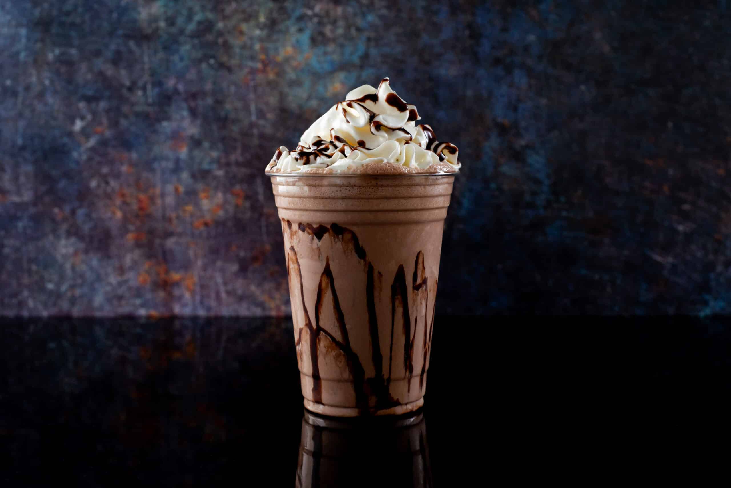 Chocolate milkshake served in a clear glass on a dark background. Isolated drink.