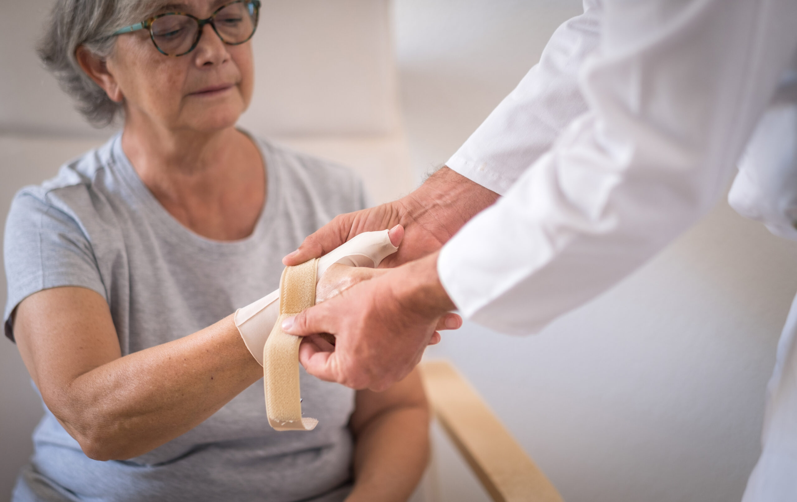 Senior female patient with rhizoarthrosis of the right thumb while wearing a thumb brace with her physical therapist. Elderly woman pain and rehabilitation at the medical center