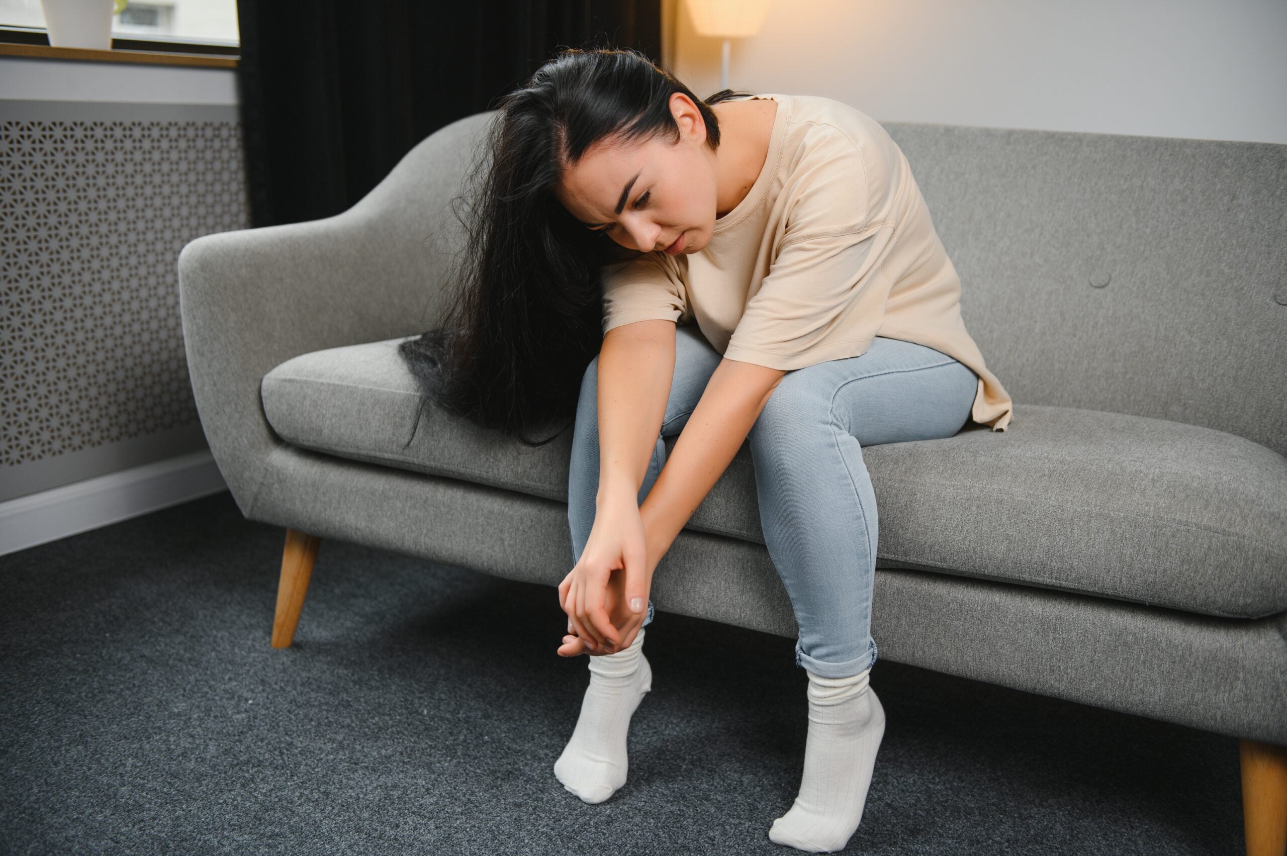 Depressed sad attractive woman crying on sofa couch at home feeling lonely tired and worried suffering depression in mental health, loneliness and isolation concept. Psychology, solitude and people