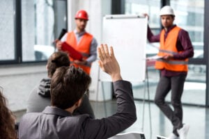 selective focus of man raising hand near handsome firemen in helmets standing near white board lost white card