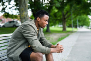 Sad and frustrated young black man sitting on bench outdoors in city, black lives matter concept. men's health week