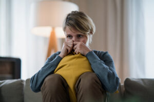 Worried woman with tablet indoors on sofa at home feeling stressed, mental health concept. Anxiety