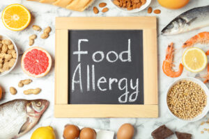 Chalkboard with words FOOD ALLERGY and different products on white marble table, flat lay food allergy first aid