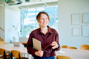 Professional woman smiling, holding a tablet and glasses, standing confidently in a bright, contemporary office environment Early Childhood Educators Day 2026