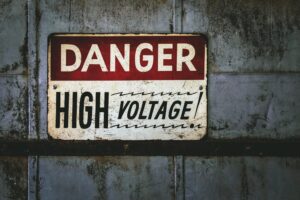A closeup of a sign with "DANGER HIGH VOLTAGE" on a grungy rusty metallic background