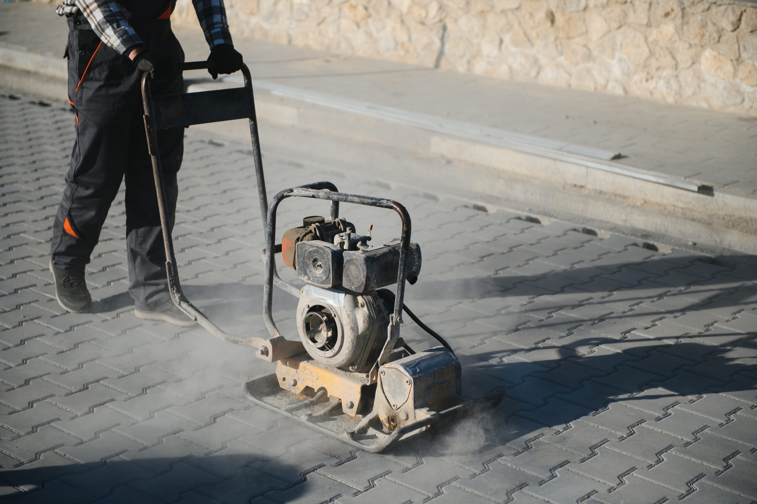 Male Worker using vibratory plate compactor to firm soil at worksite. builder. After laying of paving slabs, compacts paving stones with a gasoline vibratory compactor for subsequent. white card for paving jobs
