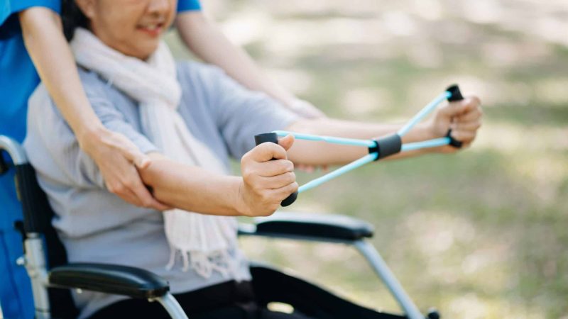 Physiotherapist helping elderly patient stretching arm during exercise correct with dumbbell in hand during training hand with patient