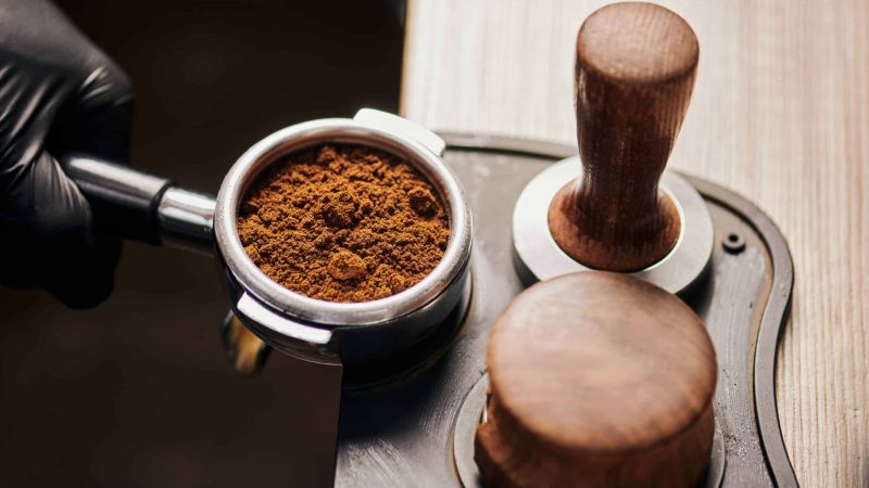 barista holding portafilter with grinded coffee, tamper