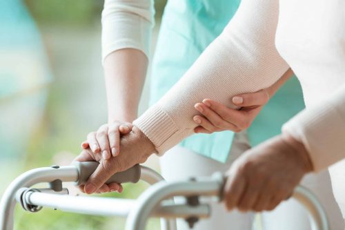 A disability support worker assists someone with a mobility aid.