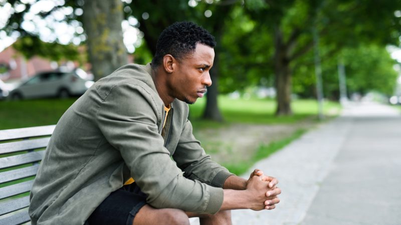 Sad and frustrated young black man sitting on bench outdoors in city, black lives matter concept. men's health week