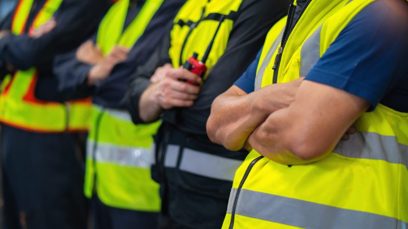 group of men in yellow safety vests stand together. They are all wearing the same type of vest and are all wearing the same color. thank a first responder day