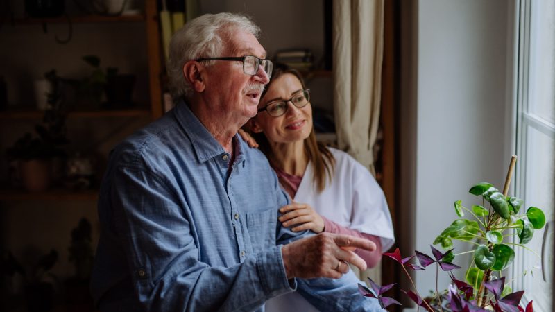 A healthcare worker or caregiver visiting senior man indoors at home, talking. dementia aged care