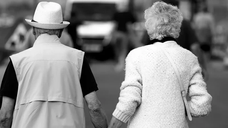 A black and white image of the backs of an older couple walking together.