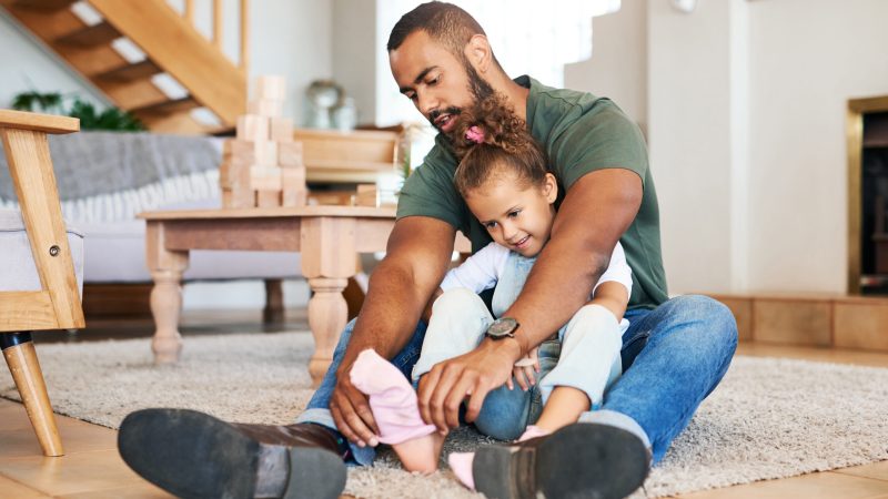 Shot of a father helping his daughter put socks on her feet at home. fathers' day