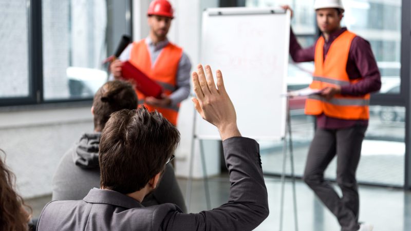 selective focus of man raising hand near handsome firemen in helmets standing near white board lost white card