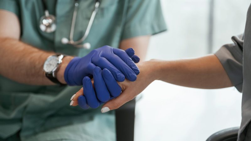 Blue gloves. Two doctors are holding hands indoors. World Patient Safety Day 2026