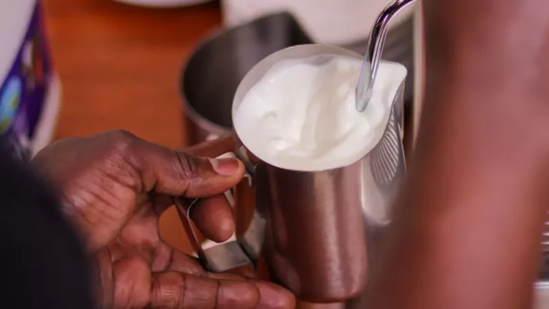 Barista frothing milk in a cafe with milk wand immersed in the warm milk