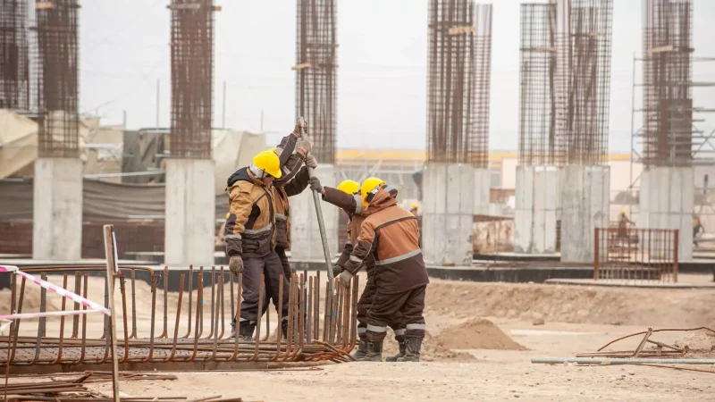 Three workers in special equipment and yellow helmets with factory construction in the background