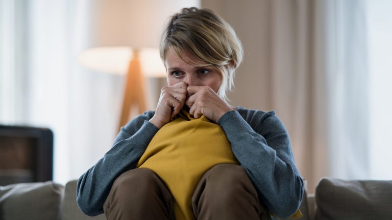 Worried woman with tablet indoors on sofa at home feeling stressed, mental health concept. Anxiety